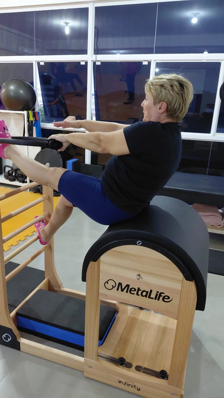 Cliente acima dos 45 anos realizando exercício de fortalecimento de coluna no barril de Pilates no Instituto AS